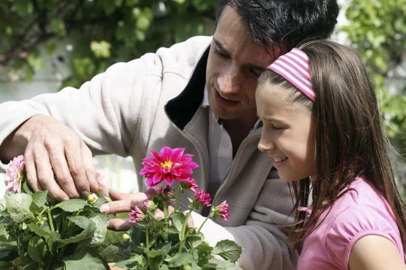 Father showing daughter how to prune flowers and grow garden