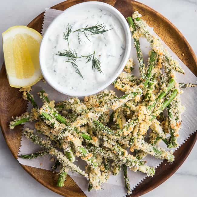 Asparagus fries on wooden tray with dipping sauce in bowl.