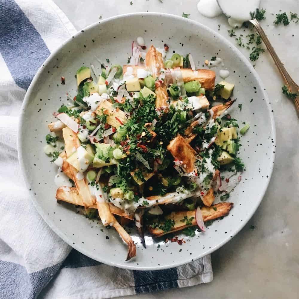 Parsnip fries with toppings on a white plate.