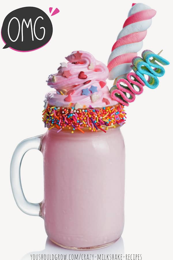 Strawberry crazy milkshake with pink whipped cream topping, twisty popsicle, candy, and sprinkles on rim of mason jar mug